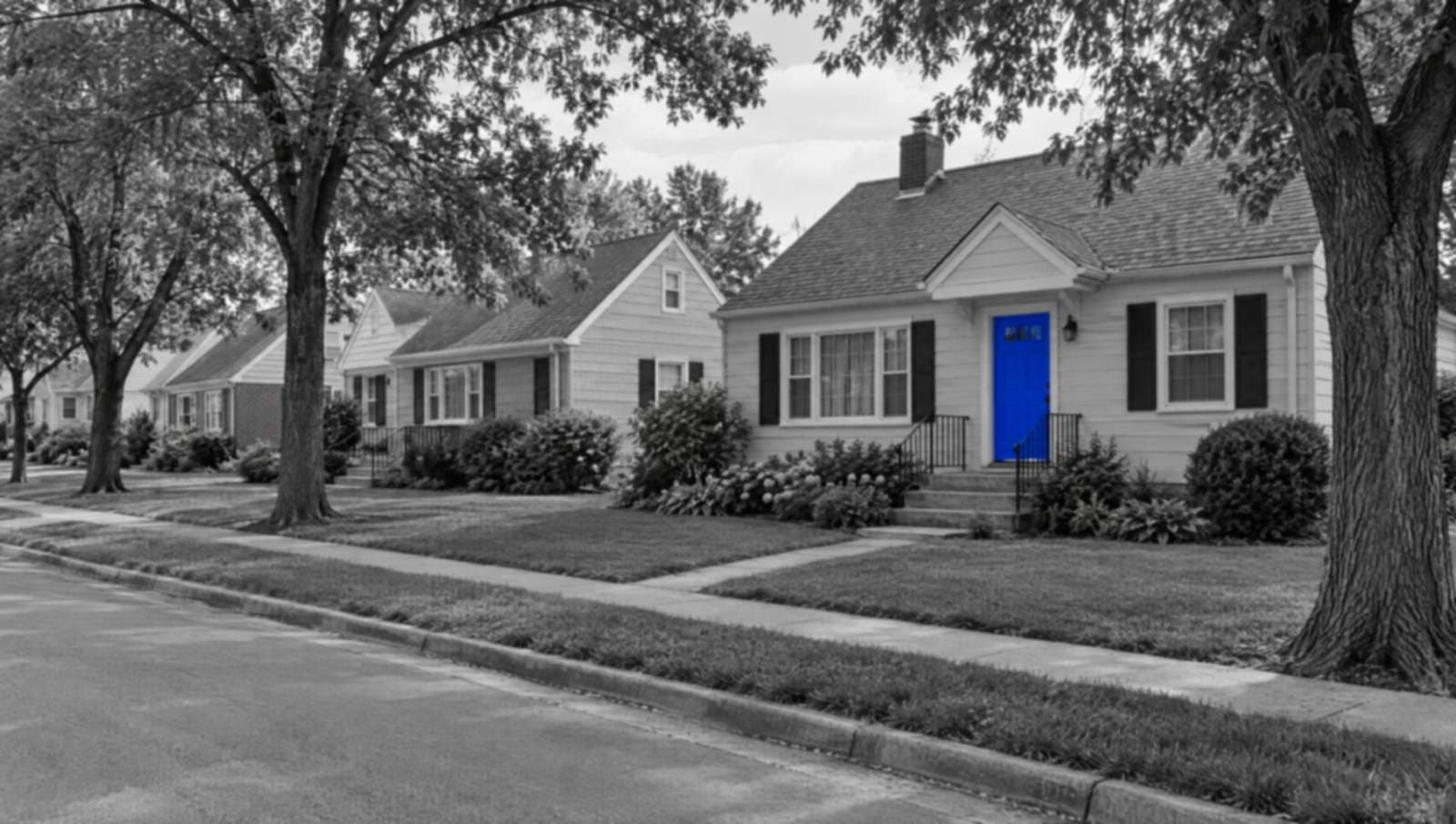 A quiet suburban street of modest homes in black and white, with one front door painted bright blue.