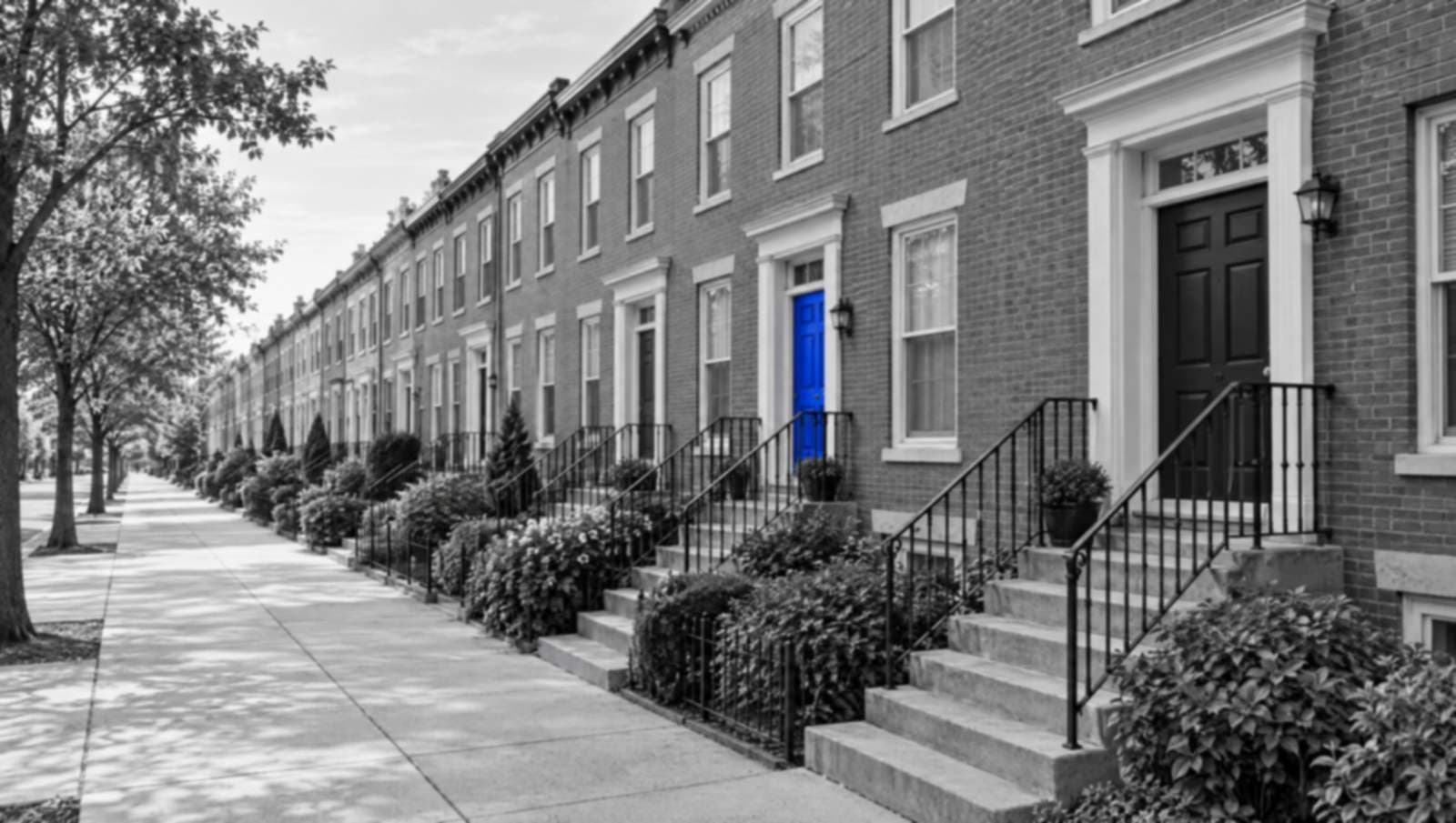A long row of townhouse front doors and stoops in black and white. One door partway down the row is bright blue.