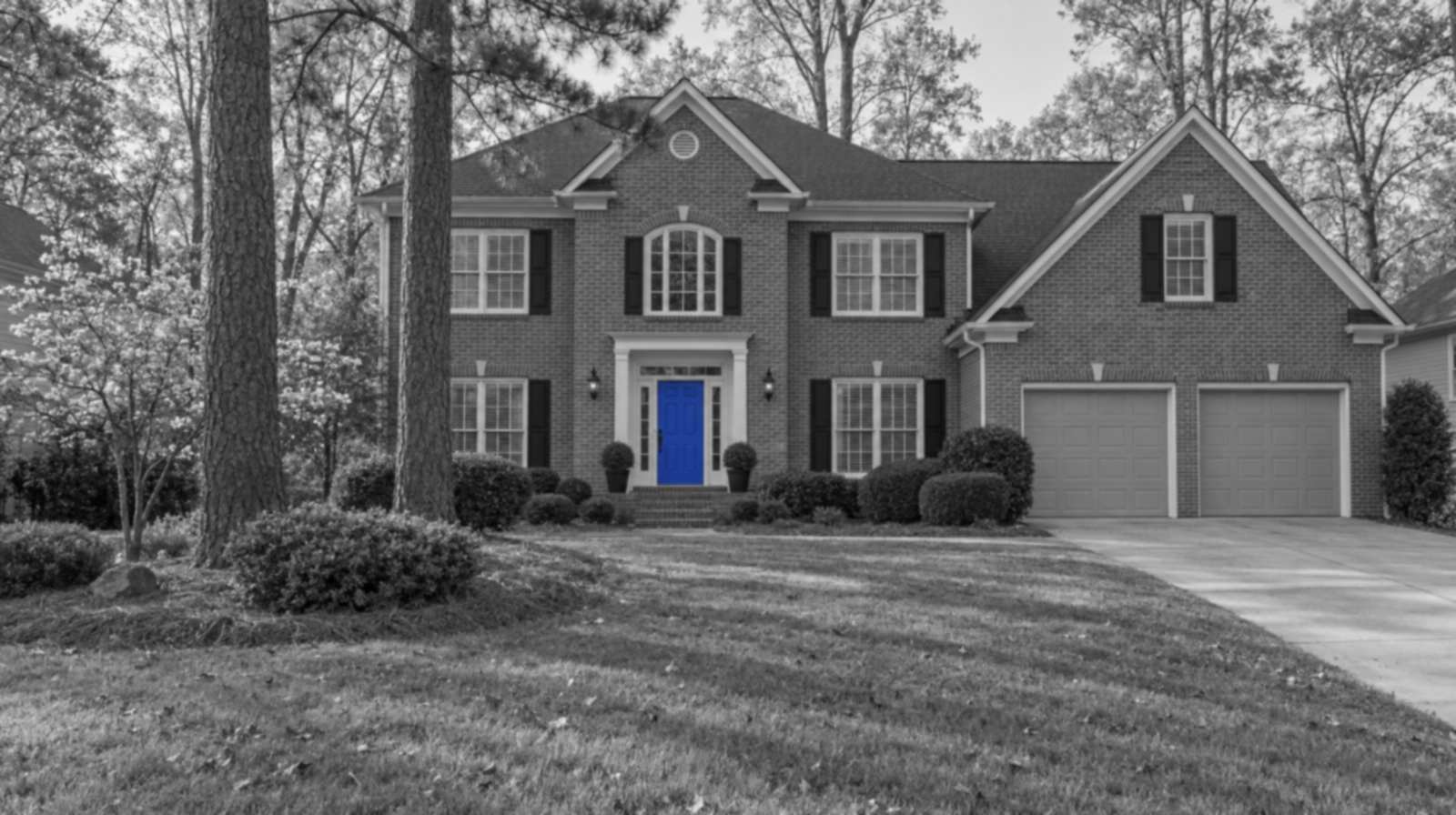 Black-and-white photo of a two-story red brick house in Marietta, Georgia, with tall pines, a flowering dogwood, pine straw beds, a two-car garage and a bright blue front door.