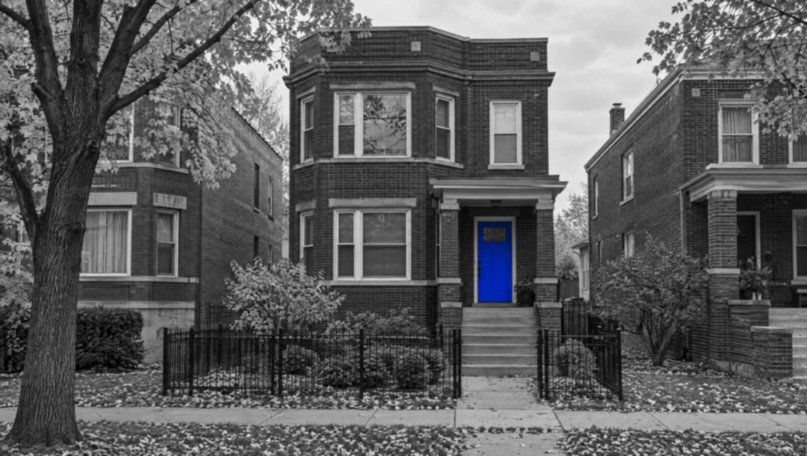 Black-and-white photo of a brick Chicago two-flat on a quiet, tree-lined street. The front door is bright blue.