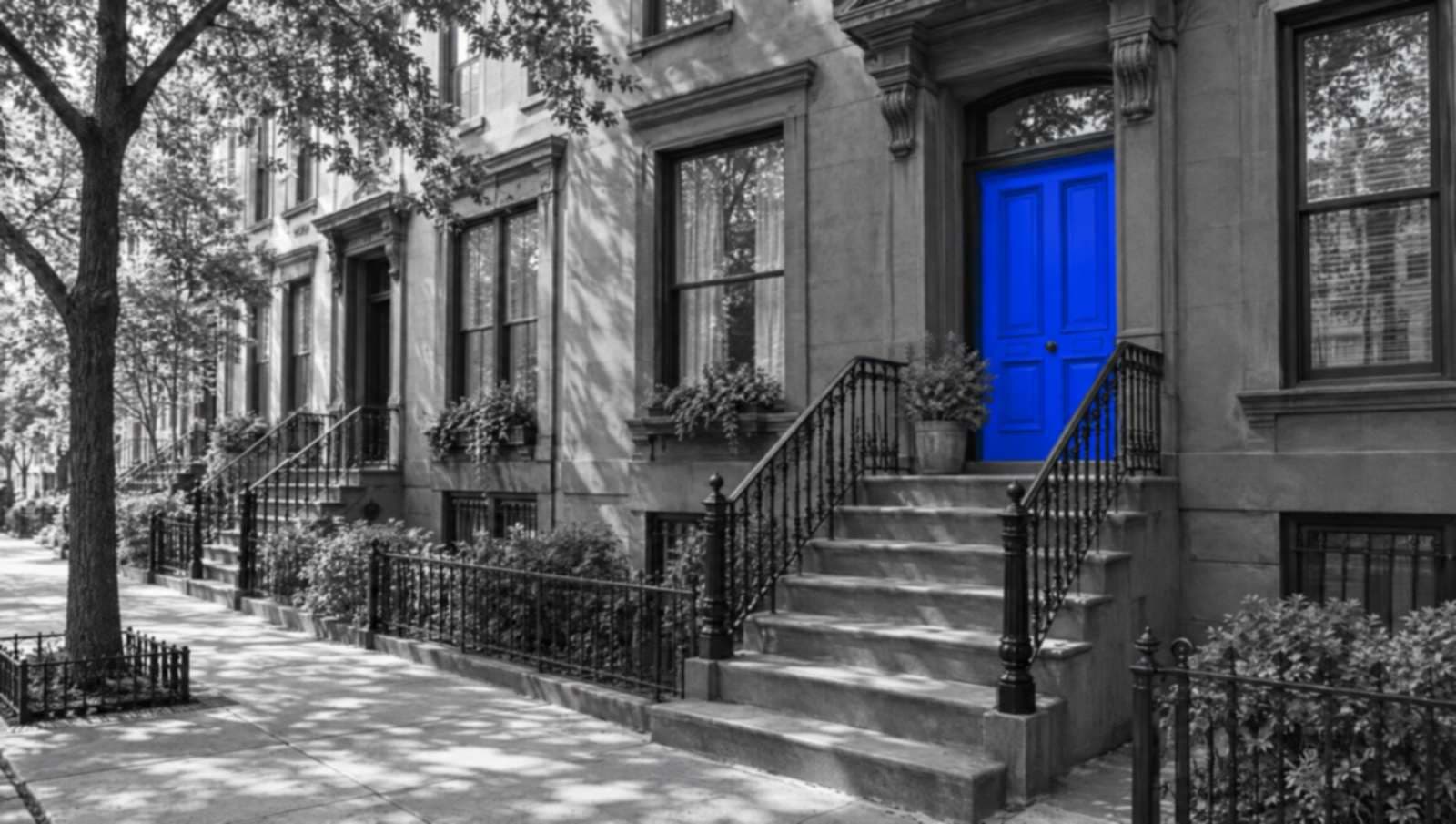 Black-and-white photo of a Brooklyn brownstone stoop with iron railings. The front door is bright blue.