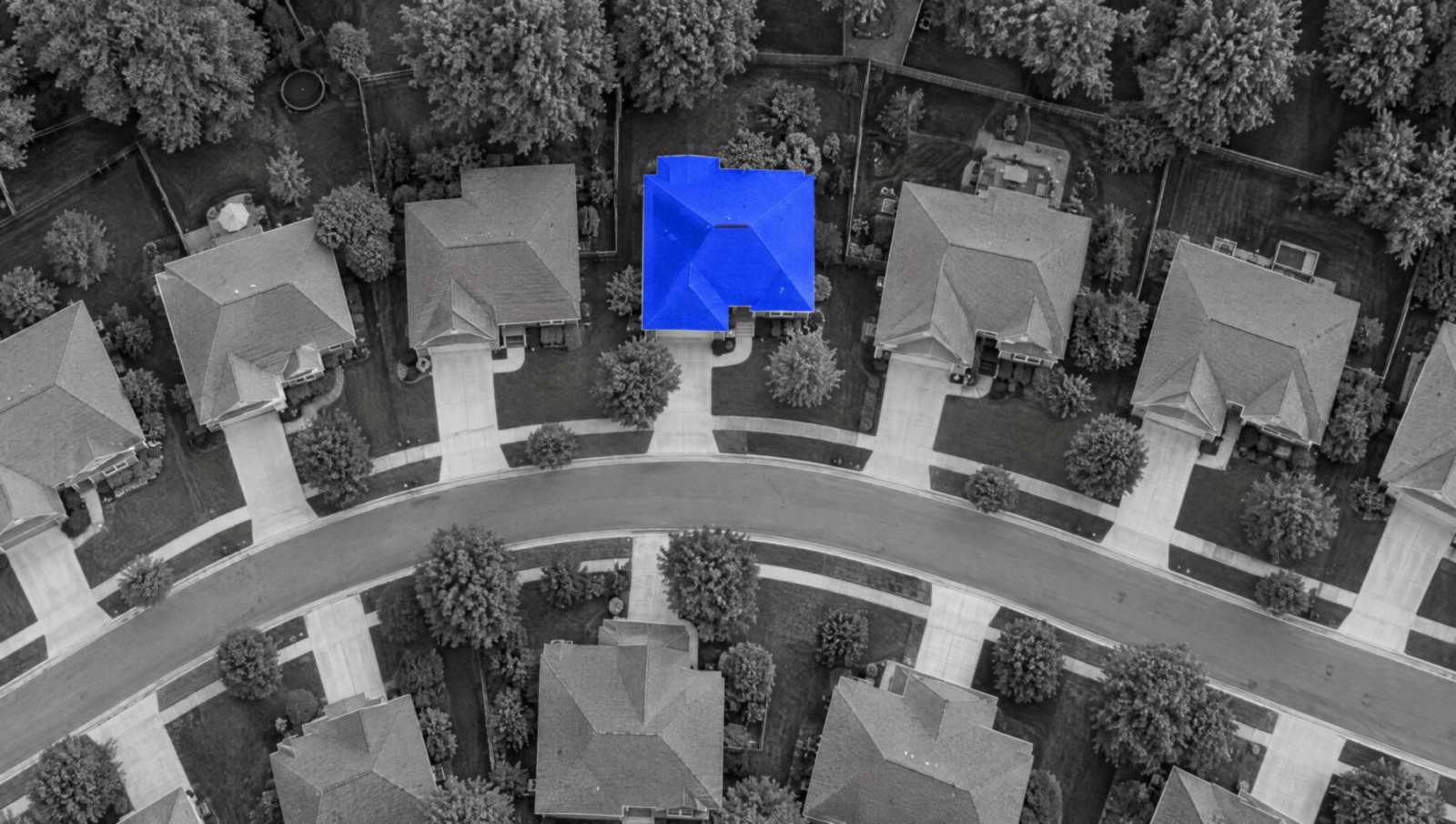 An aerial view of a curving suburban street in black and white, where one house has a bright blue roof.