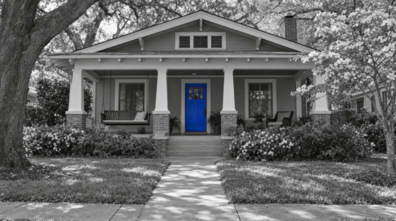 Black-and-white photo of a Decatur, Georgia craftsman bungalow with a porch swing, oak and dogwood trees, and a bright blue front door