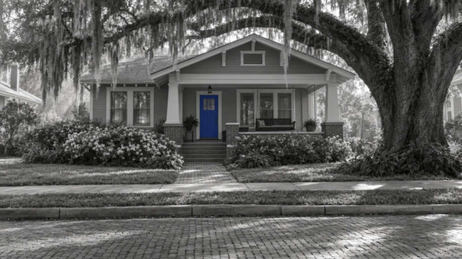 Black-and-white photo of a Jacksonville craftsman bungalow under a live oak hung with Spanish moss, with a brick street in front. The front door is bright blue.