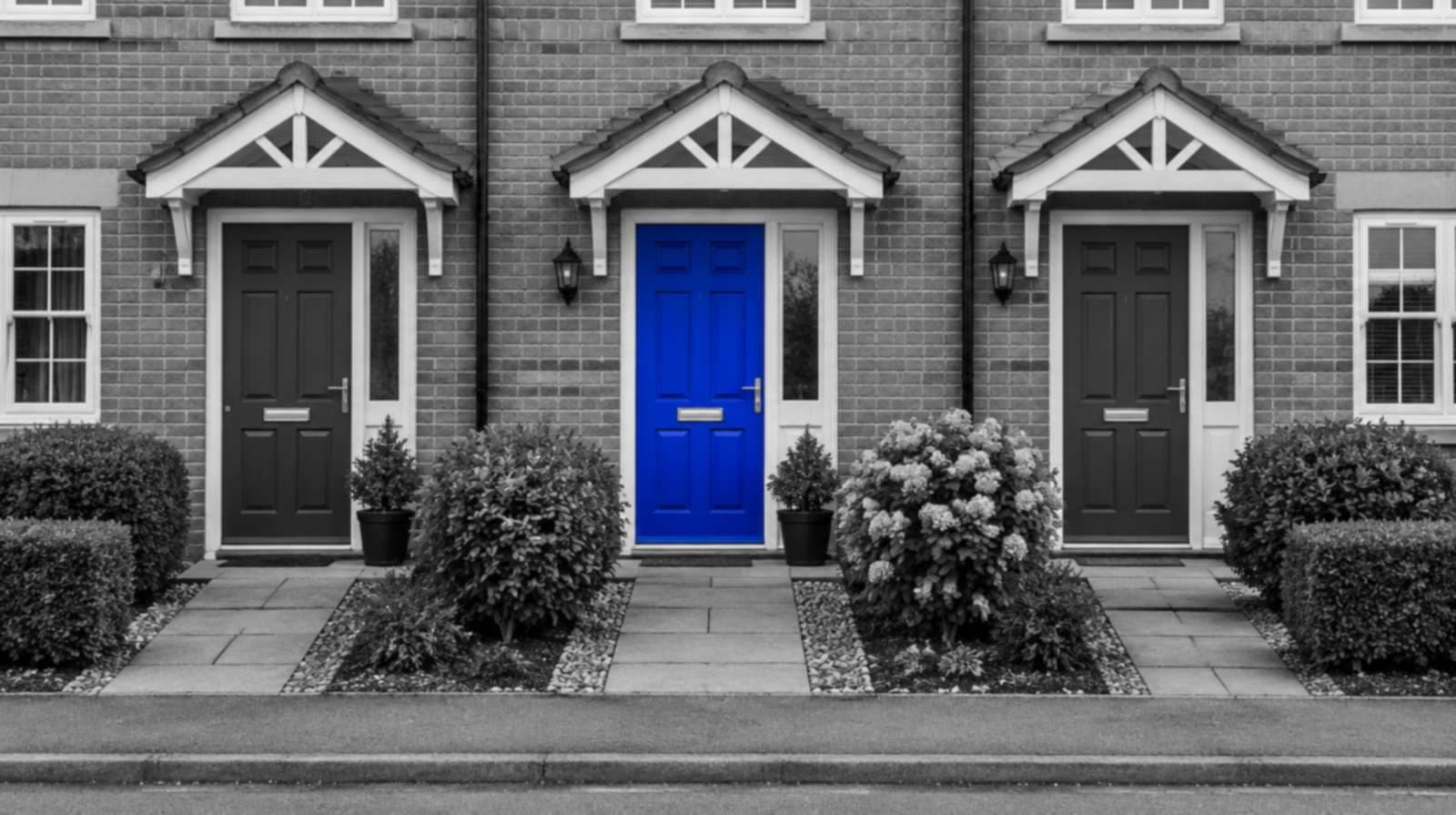 Three front doors side by side on a row of townhouses, in black and white. The middle door is bright blue.