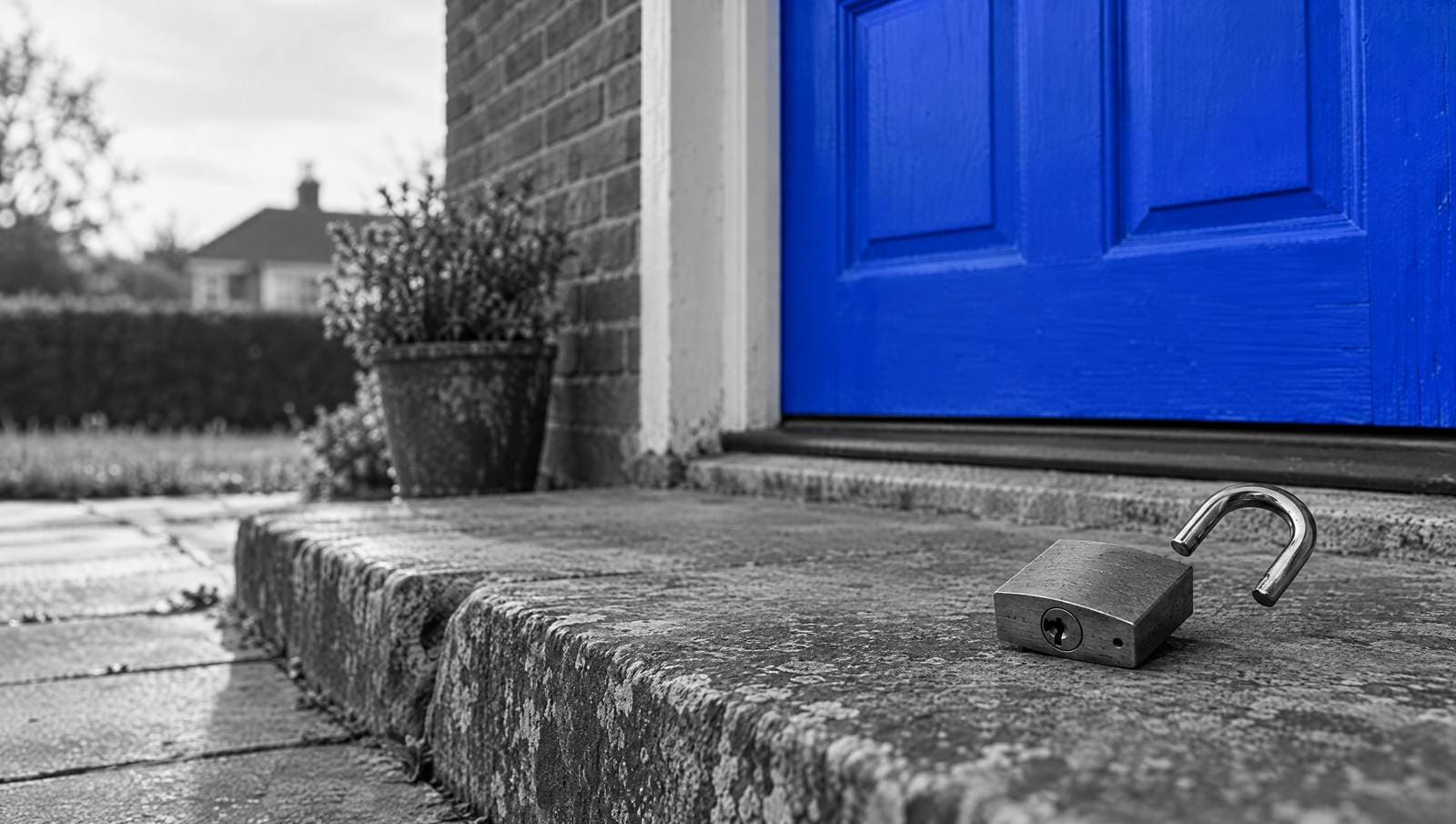 An open padlock resting on a stone doorstep in front of a blue front door, in a black-and-white photo.